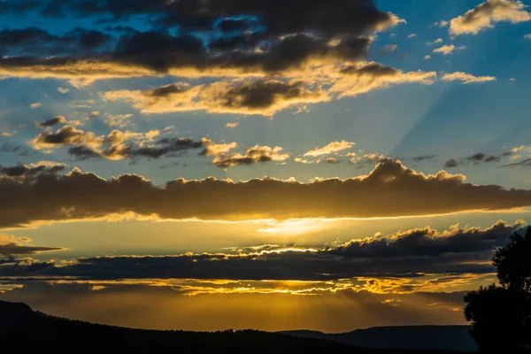 Sunset on a day with clouds and sun rays coming out of them in the mountain.