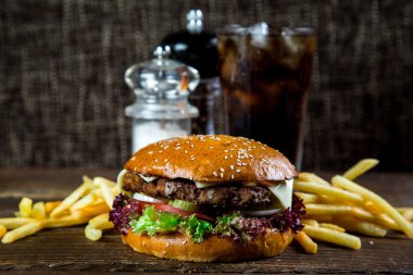 Kola ve koyu arka plan üzerinde patates kızartması ile masa üzerinde büyük ve lezzetli hamburger