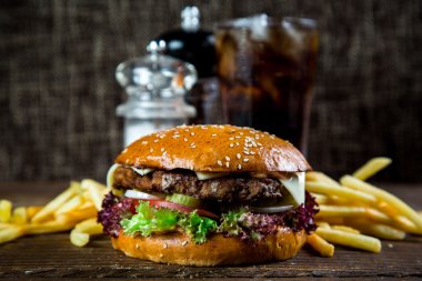 Kola ve koyu arka plan üzerinde patates kızartması ile masa üzerinde büyük ve lezzetli hamburger