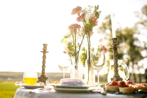 精美奠定了节日的餐桌在花园里的两个手持鲜花和蜡烛 — 图库照片