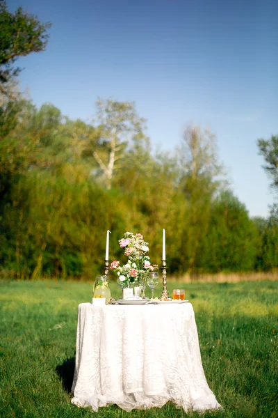 精美奠定了节日的餐桌在花园里的两个手持鲜花和蜡烛 — 图库照片