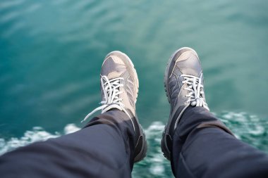 Denizin arka planında spor ayakkabılı bacaklar 
