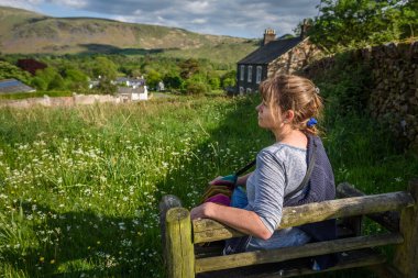 Çekici orta yaşlı bir kadın güneş ışığında bankta oturmuş Wasdale, Cumbria, Lake District Ulusal Parkı manzarasının keyfini çıkarıyordu..