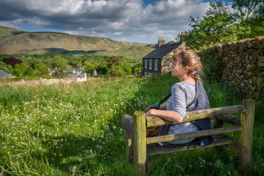 Çekici orta yaşlı bir kadın güneş ışığında bankta oturmuş Wasdale, Cumbria, Lake District Ulusal Parkı manzarasının keyfini çıkarıyordu..