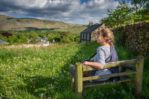 Çekici orta yaşlı bir kadın güneş ışığında bankta oturmuş Wasdale, Cumbria, Lake District Ulusal Parkı manzarasının keyfini çıkarıyordu..