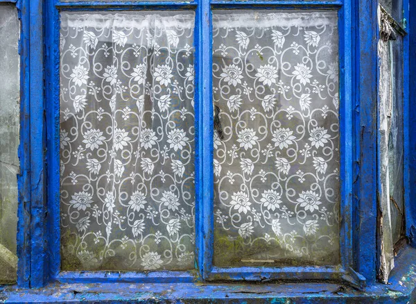 Yıpranmış pencere çerçeveleri ve ağ perdeleri olan terk edilmiş eski bir ev..