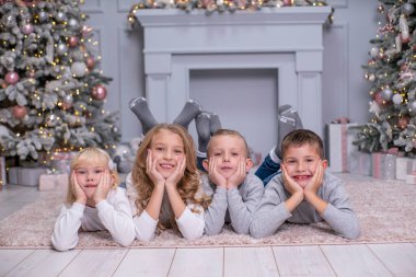 İki erkek ve iki kız halının üzerinde uzanmış Noel dekoru olan bir odada gülümsüyorlar. Birbirinizi sevin.