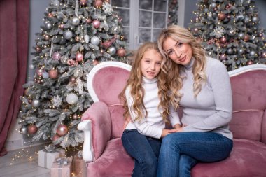 Anne ve kızı Noel arkaplanında koltukta oturuyor..