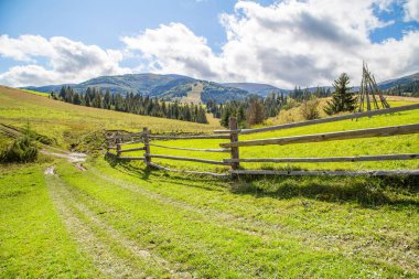 Açık bir yaz gününde dağlarda kırsal kesimde. Ahşap çitlerin yanındaki yol, dağlık arazinin arka planında..
