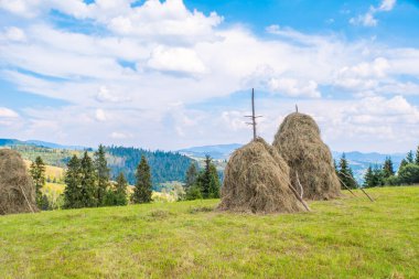 Tepedeki saman yığını. Dağlardaki kırsal alan. Vadideki köy. Güneşli bir yaz gününde gökyüzünde kabarık bulutlar...