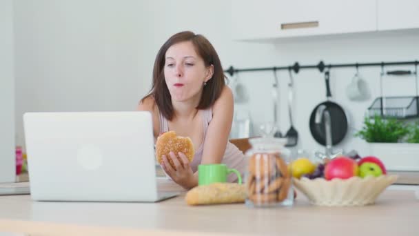 Mujer come hamburguesa y trabaja con el ordenador portátil — Vídeos de Stock