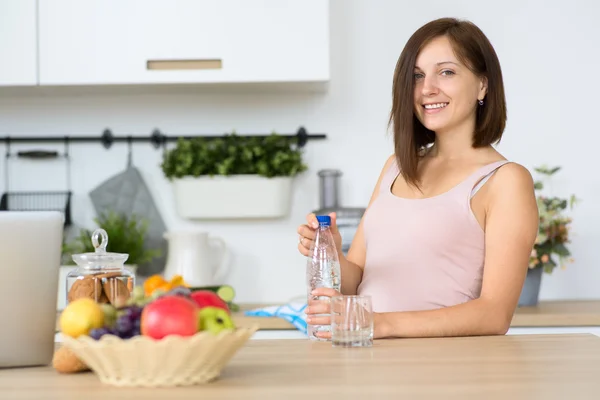 Mujer sonriente con botella de agua en la cocina — Foto de Stock