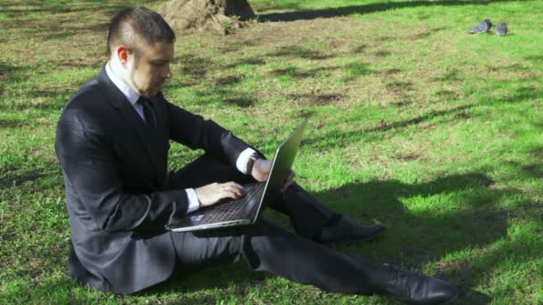 Empresario trabaja con portátil en el parque de la ciudad — Vídeos de Stock