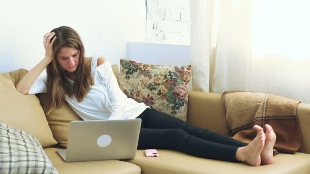 Νεαρή γυναίκα που χρησιμοποιεί φορητό υπολογιστή στον καναπέ — Αρχείο Βίντεο