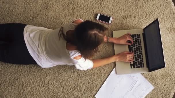Fiatal barna feküdt a szőnyegen, és használ laptop — Stock videók