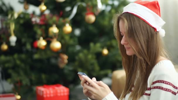 Pretty girl in christmas cap using smartphone — Stock Video