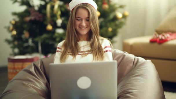 लैपटॉप का उपयोग करके क्रिसमस टोपी में सुंदर लड़की — स्टॉक वीडियो
