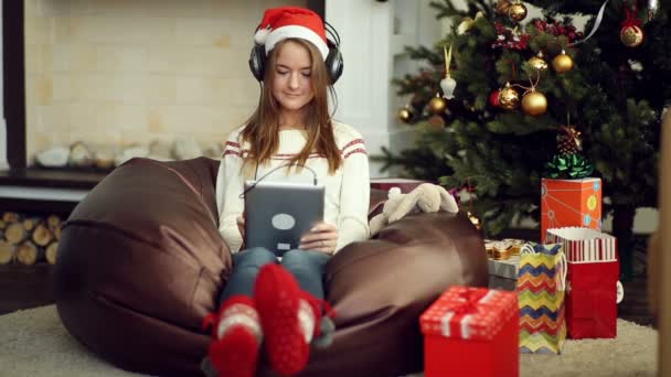 Chica bastante joven en brillantes calcetines de Navidad con almohadilla y escuchar música — Vídeos de Stock