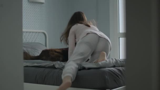 Молода усміхнена жінка лежить зі своєю собакою в ліжку . — стокове відео