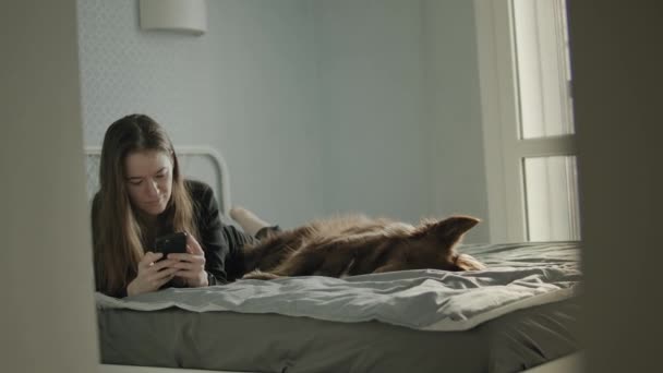 Młoda kobieta w domu za pomocą smartfona blisko jej psa. — Wideo stockowe