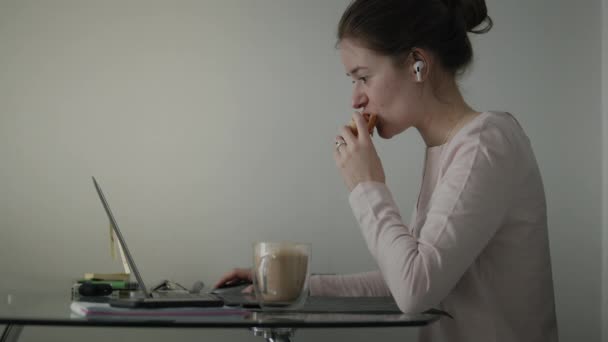 Mujer come su desayuno Cerca de Ordenador Portátil — Vídeos de Stock