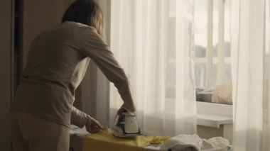 Genç kadın evde ütü yapıyor.