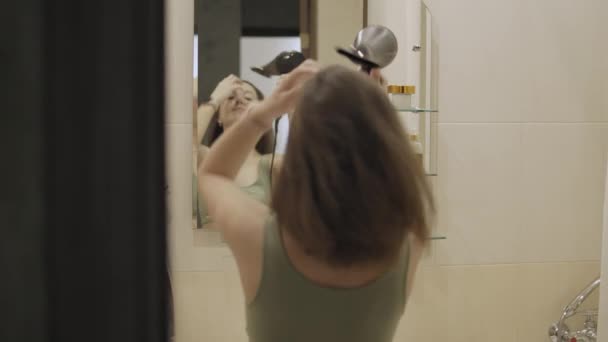 Chica seca el cabello con secador de pelo en el baño. — Vídeo de stock