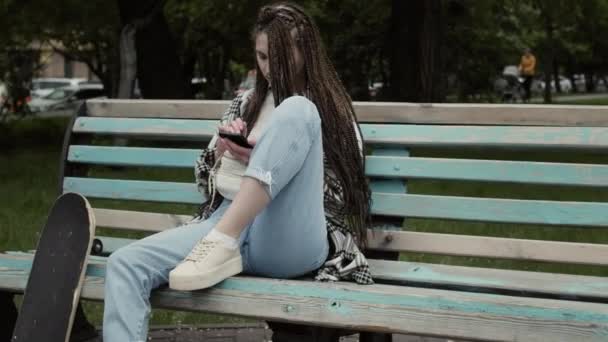 Mladý bruslař dívka textování venku. — Stock video