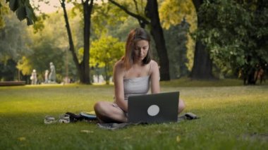 Genç bir kadın parkta dizüstü bilgisayarla çalışıyor..