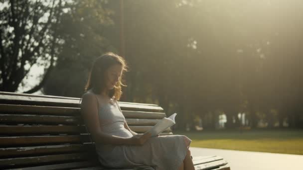 Mujer joven leyendo en el parque al atardecer — Vídeos de Stock