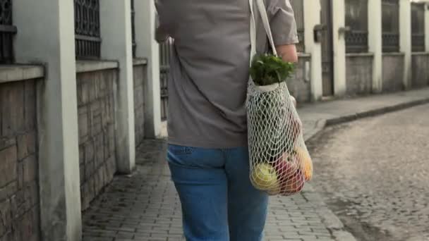 Vrouw loopt buiten met gaas koord gebreide boodschappentas — Stockvideo