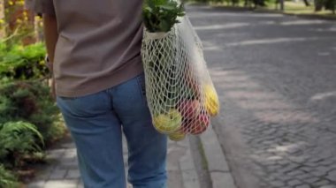 Dışarıda örgü örgülü alışveriş çantasıyla yürüyor.