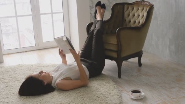 Leer un libro tumbado en el suelo — Vídeos de Stock