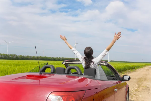 Mulher em um cabriolet vermelho em um campo com energia eólica . — Fotografia de Stock