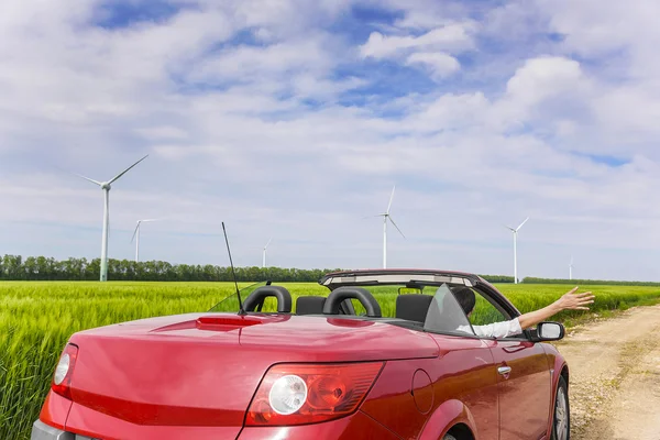 Kobieta w czerwony kabriolet w polu z elektrowni wiatrowych. — Zdjęcie stockowe