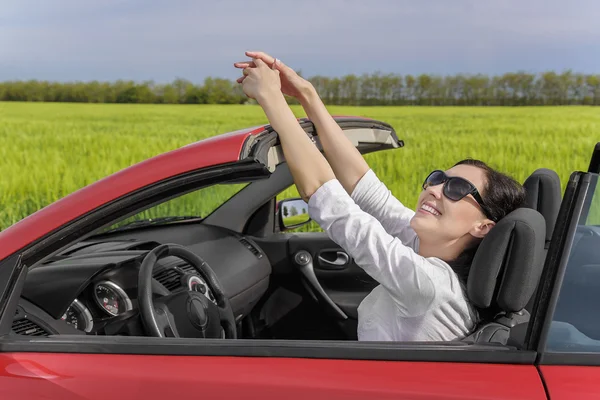 Gelukkige vrouw achter het stuur van een auto op een landweg rusten bij zonsondergang. — Stockfoto