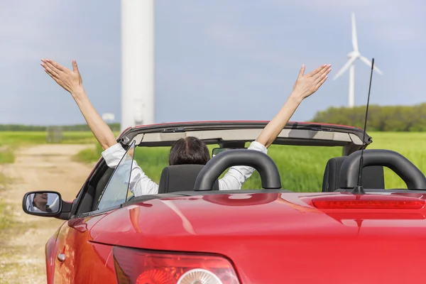 Mulher em um carro vermelho um campo com energia eólica . — Fotografia de Stock