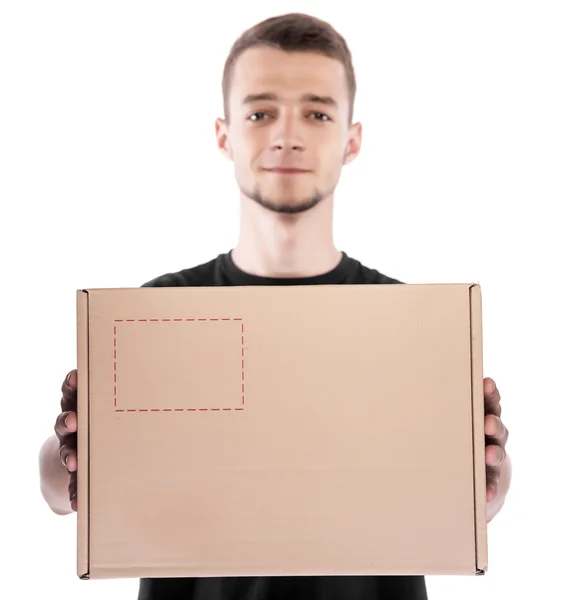 Joven repartidor sonriente sosteniendo y llevando una caja de cartón aislada sobre fondo blanco — Foto de Stock