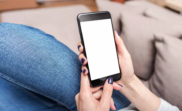 Um smartphone nas mãos de uma mulher que está no sofá. As mãos usam um smartphone. — Fotografia de Stock
