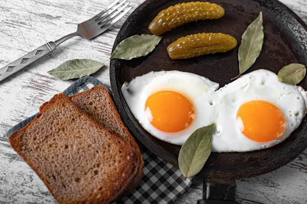 Gebratene Eier in einer Pfanne mit Scheiben Schwarzbrot und eingelegten Gurken — Stockfoto