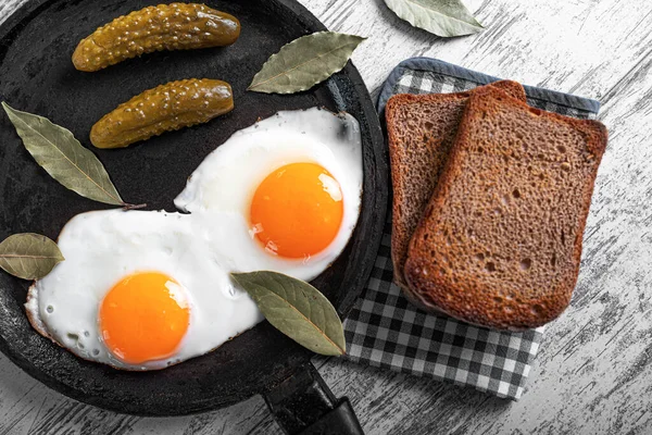 Смажені яйця на сковороді зі скибочками чорного хліба та маринованими огірками — стокове фото