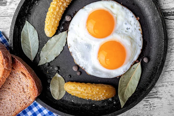 Gebratene Eier in einer Pfanne mit Scheiben Schwarzbrot und eingelegten Gurken — Stockfoto