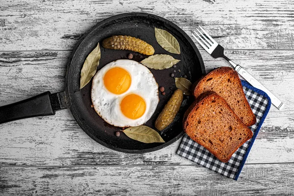 Смажені яйця на сковороді зі скибочками чорного хліба та маринованими огірками — стокове фото