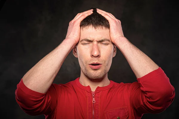 Un hombre sostiene su cabeza con la mano sobre un fondo oscuro. Dolor de cabeza, migraña, estrés — Foto de Stock