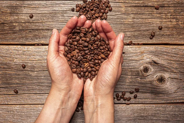 Coffee beans in hands on a wooden background — Stock Photo, Image