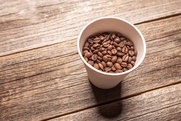 Paper cup with coffee beans on wooden table. — Stock Photo, Image