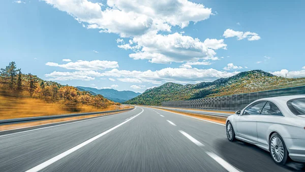 Bílé auto se řítí po silnici na pozadí krásné krajiny. — Stock fotografie