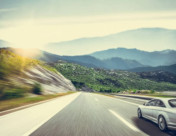White car rushes along the road against the backdrop of a beautiful countryside landscape. — Stock Photo, Image