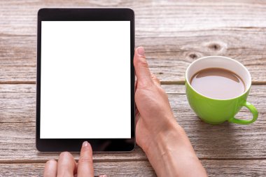 Tablet, elinde bir bardakla ahşap bir masada..