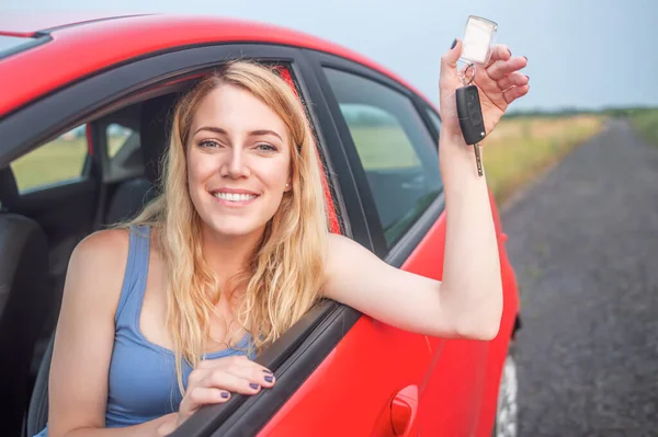 Uma mulher bonita em um carro segura uma chave de carro em suas mãos. — Fotografia de Stock